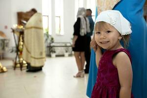 poco ragazza nel Chiesa sorrisi e sembra a il telecamera. foto