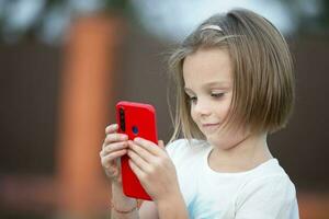 bambino con un' smartphone. il poco ragazza è parlando con un' rosso Telefono. foto