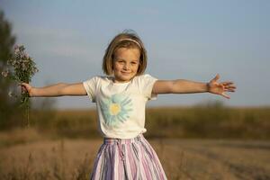 contento poco ragazza nel il prato con un' mazzo di fiori. bambino su un' bellissimo estate campo. foto