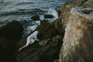 sensuale donna dire bugie su sua indietro su un' roccioso riva del mare paesaggio foto