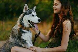 un' donna con un' rauco razza cane sorrisi e affettuosamente colpi sua Amati cane mentre a piedi nel natura nel il parco nel autunno contro il fondale di tramonto foto