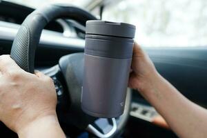 asiatico donna autista hold termo boccale con caldo caffè nel macchina, pericoloso e rischio un incidente. foto