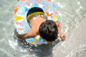 contento indiano ragazzo nuoto nel un' piscina, ragazzo indossare nuoto costume lungo con aria tubo durante caldo estate vacanze, bambini ragazzo nel grande nuoto piscina. foto