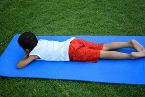 asiatico inteligente ragazzo fare yoga posa nel il società parco all'aperto, figli di yoga posa. il poco ragazzo fare yoga e meditazione esercizio. foto