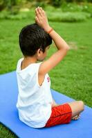 asiatico inteligente ragazzo fare yoga posa nel il società parco all'aperto, figli di yoga posa. il poco ragazzo fare yoga e meditazione esercizio. foto