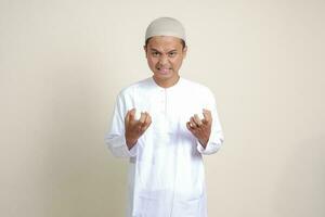ritratto di attraente asiatico musulmano uomo nel bianca camicia fabbricazione arrabbiato mano gesto con dita. isolato Immagine su grigio sfondo foto