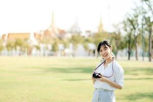 ritratto di asiatico donna viaggiatore utilizzando telecamera. Asia estate turismo vacanza concetto con il mille dollari palazzo nel un' sfondo a bangkok, Tailandia foto