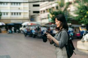 giovane asiatico donna zaino viaggiatore utilizzando digitale compatto telecamera, godendo strada culturale Locale posto e Sorridi. viaggiatore controllo su lato strade. foto