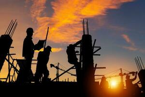 silhouette di ingegnere e lavoratore squadra controllo progetto a edificio luogo sfondo, costruzione luogo con tramonto nel sera tempo sfondo foto