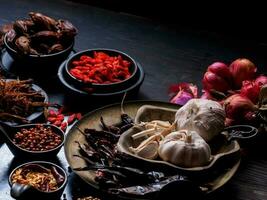 foto vista dall'alto un sacco di aglio, cipolle, peperoni, peperoncino ed erbe secche, sono stati posti su piatti e tazze su uno sfondo nero di legno drak. è stato diviso per preparare a cucinare cibo india cibo sano