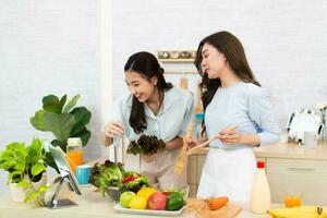 Due giovane asiatico donne siamo lettura ricetta a partire dal il digitale tavoletta nel il cucina. donna avendo divertimento con salutare cibo insalata. foto