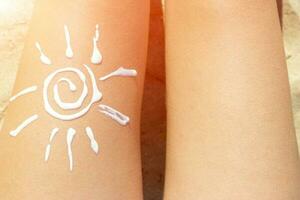 donna prendere il sole su il spiaggia con un' disegno di sole su sua gamba con crema foto