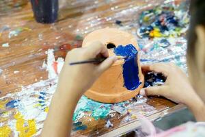 asiatico poco ragazza studia e apprendimento dipingere su fiore pentola nel il arte aula di sua scuola. foto