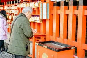 kyoto, Giappone, 2018 - il asiatico vecchio uomo siamo pagare omaggio per Budda statua nel il rosso santuario a fushimi inari santuario. il culto di il Budda è un' rispetto per Budda immagini di buddisti. foto