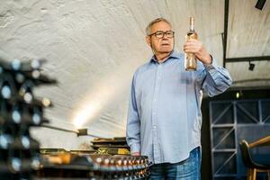 ritratto di anziano uomo chi possiede azienda vinicola. lui è l'esame qualità nel il suo vino cantina. industria vino fabbricazione concetto. foto