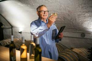 ritratto di anziano uomo chi possiede azienda vinicola. lui è l'esame qualità nel il suo vino cantina. industria vino fabbricazione concetto. foto