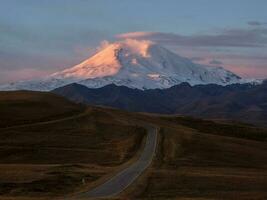 il itinerario per il alba elbrus. rosa maestoso alba al di sopra di montare elbrus. nevoso montagna picchi a alba. tramonto nel magenta toni. atmosferico viola paesaggio con un' alta altitudine nevoso montagna valle. foto