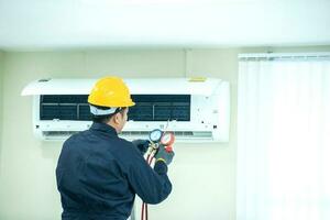 un asiatico giovane tecnico servizio uomo indossare blu uniforme controllo, professionale aria condizionatore installatore mantenimento moderno interno aria condizionatore spazio per testo foto