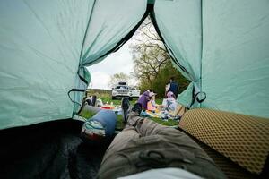 padre gambe a partire dal tenda. contento giovane famiglia, madre e bambini avendo divertimento e godendo all'aperto su picnic coperta pittura a giardino primavera parco, rilassamento. foto