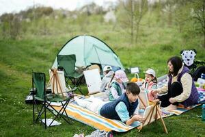 contento giovane famiglia, madre e quattro bambini avendo divertimento e godendo all'aperto su picnic coperta pittura a giardino primavera parco, rilassamento. foto