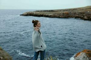 donna nel un' grigio maglione sta su un' roccioso riva natura stile di vita foto