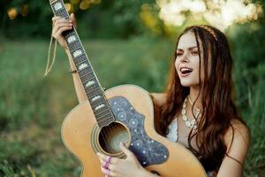 bellissimo donna giocando chitarra nel natura nel un' hippie estate Guarda, cantando canzoni stile di vita senza preoccupazioni foto