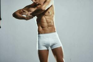 sportivo uomo con pompato su muscolare corpo nel bianca pantaloncini allenarsi leggero sfondo foto