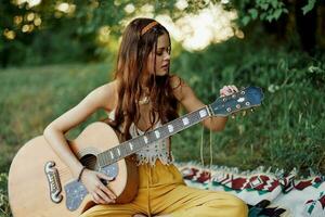 contento hippie donna con un' chitarra sorrisi seduta nel natura di il lago foto