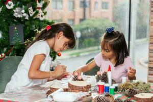 Due poco sorelle avendo divertimento mentre fabbricazione Natale Natività mestieri con a casa - vero famiglia foto