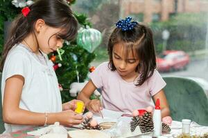 Due poco sorelle avendo divertimento mentre fabbricazione Natale Natività mestieri con a casa - vero famiglia foto