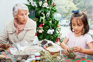 poco ragazza avendo divertimento mentre fabbricazione Natale Natività mestieri con sua nonna - vero famiglia foto