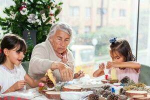 poco ragazze avendo divertimento mentre fabbricazione Natale Natività mestieri con loro nonna - vero famiglia foto