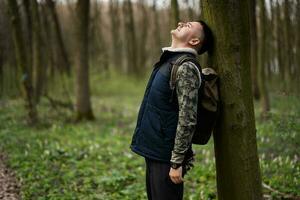 ritratto di uomo con zaino Appoggiato il suo indietro contro un' albero su foresta. amore per natura. foto