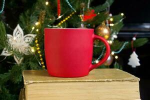 vuoto rosso boccale con Natale albero su sfondo, stuoia tè o caffè tazza con Natale e nuovo anno decorazione, verticale finto su con ceramica boccale per caldo bevande, vuoto regalo Stampa modello foto