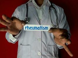 un' medico in piedi, hold il reumatismo carta testo su rosso sfondo. medico e assistenza sanitaria concetto. foto