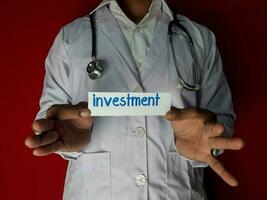 un' medico in piedi, hold il investimento carta testo su rosso sfondo. medico e assistenza sanitaria concetto. foto