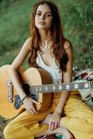 contento hippie donna con un' chitarra sorrisi seduta nel natura di il lago foto