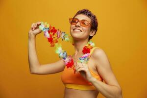 donna con floreale hawaiano ghirlanda in giro sua collo ha divertimento danza e sorridente nel luminosa capi di abbigliamento contro un arancia sfondo foto