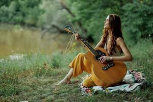 un' hippie donna giocando sua chitarra sorrisi e canta canzoni nel natura seduta su un' plaid nel il sera nel il tramonto luce del sole. un' stile di vita nel armonia con il corpo e natura foto