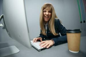 il male irritata del Millennio bionda donna d'affari lavoratore nel blu giacca pause tastiera odiare operazione schianto nel grigio moderno ufficio. a distanza lavoro, tecnologia e carriera professione concetto. largo angolo foto