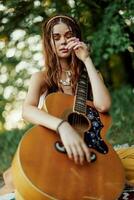 un' giovane hippie donna con un' chitarra nel sua mani sorrisi dolcemente in il telecamera su un' viaggio per natura stile di vita nel armonia foto