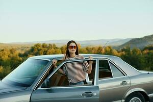 un' giovane donna autista sembra su di il auto a il autunno paesaggio e sorrisi in modo soddisfacente foto