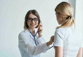 donna pulizia signora nel un' medico toga ascolta per il del paziente battito cardiaco su un' leggero sfondo foto