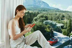 ritratto di bellissima donna uso il Telefono sembra a il schermo nel un' confortevole Hotel un Aperto Visualizza di il Perfetto foto