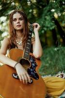 un' giovane hippie donna con un' chitarra nel sua mani sorrisi dolcemente in il telecamera su un' viaggio per natura stile di vita nel armonia foto