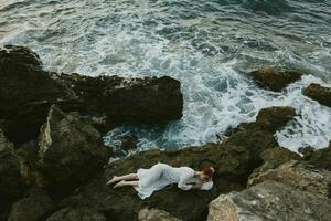 bellissimo sposa nel lungo bianca vestito bagnato capelli dire bugie su un' roccioso scogliera natura paesaggio foto