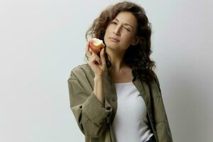 una delizia esso. carino fanny allegro Riccio bellissimo donna nel casuale cachi verde camicia mangiare Mela strizza l'occhio a voi in posa isolato su al di sopra di bianca sfondo. naturale eco-friendly prodotti concetto. copia spazio foto