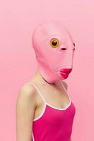 divertente pazzo donna su un' rosa sfondo in piedi nel un' pesce testa maschera su un' rosa sfondo, concettuale Halloween costume arte foto