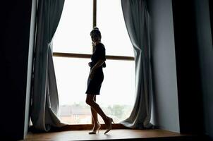 donna vicino il finestra nel nero vestito e in posa foto