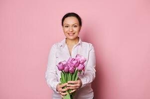 sorridente donna con rosa consapevolezza nastro, Tenere su a telecamera un' mazzo di tulipani, supporto Seno cancro sopravvissuti foto
